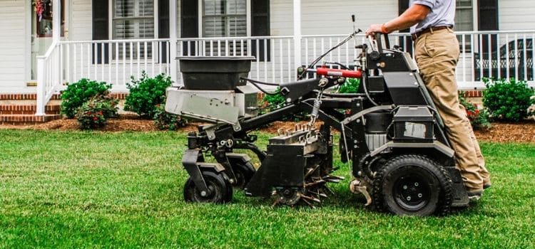 Commercial stand-on aerator performing service on residential lawn.