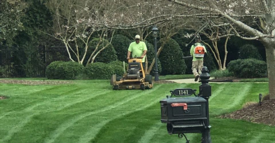 An ECM employee on a commercial mower mowing a lawn while the other employee is blowing off the grass clippings.