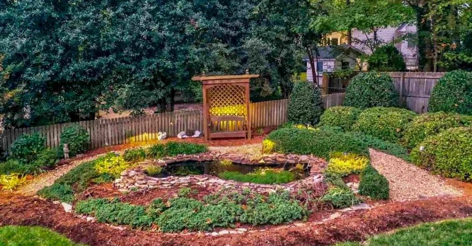 Mulched landscape bed with plants, pond, and seating area.